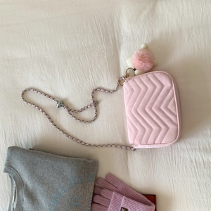 Detailaufnahme der rosa Stepptasche mit Metallkettenriemen und Plüschkugel-Anhänger