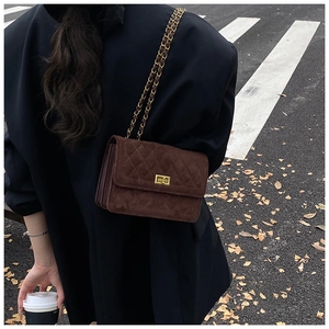 Detail of brown quilted suede crossbody bag with gold chain strap and metal turn-lock