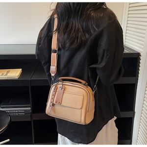Beige pebble leather crossbody bag with wide woven strap shown in a lifestyle setting