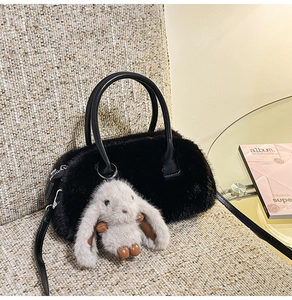 Detail of black faux fur handbag featuring leather handles and a grey rabbit charm