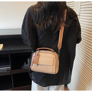 Rear view of a beige lychee pattern crossbody bag with a wide strap on a model