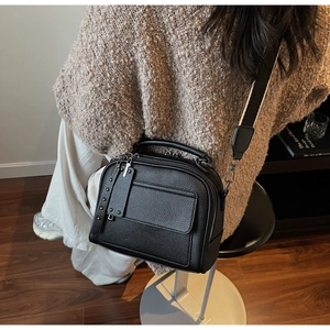 Close-up of black litchi pattern crossbody bag featuring retro rivets and wide strap