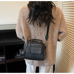 Detailed view of a black lychee texture crossbody bag with wide strap on a model back