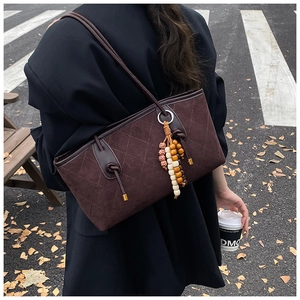 Detail of dark caramel suede tote bag with quilted diamond pattern and wooden bead charm