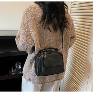 Detailed view of black litchi grain crossbody bag with wide strap on model