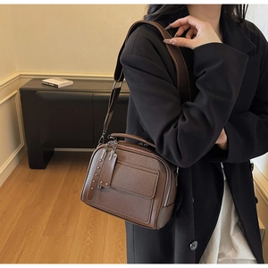 Detail view of brown leather crossbody bag with litchi texture and wide strap on model