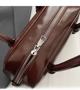 Detailed close-up of a smooth silver metal zipper on a dark brown glossy leather bag