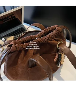Detail of the magnetic clasp and drawstring closure on a brown suede bucket bag