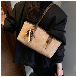 Detail of beige quilted canvas shoulder bag with brown leather trim and beaded tassel