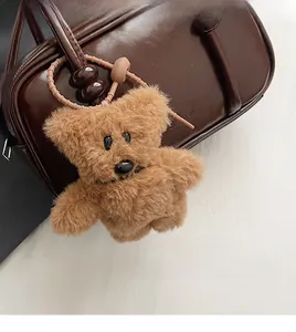 Close-up of a brown plush bear charm with a pink bead chain on a dark patent handbag