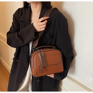 Detailed shot of brown lychee leather crossbody bag featuring wide strap and twin zippers