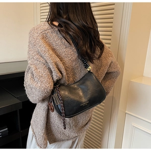 Detailed view of the black leather textured shoulder bag with woven pendant on model