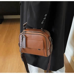 Close-up of vintage brown leather crossbody bag with wide strap and metallic hardware details