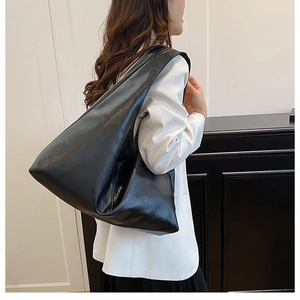 Detail view of black soft leather tote bag with wide shoulder strap on a model
