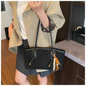 Detail of black quilted tote bag featuring retro wooden bead charm and slim shoulder straps