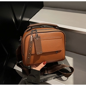Detail of dark brown lychee grain leather crossbody bag with wide strap and rivet accents