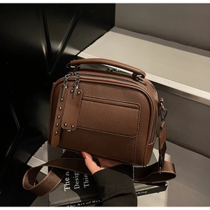 Detail of dark brown litchi pattern leather camera bag with wide woven strap and silver rivets