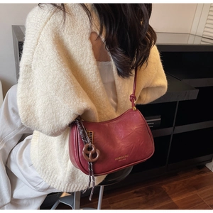 Detail of burgundy leather shoulder bag showing gold brand logo and round charm pendant