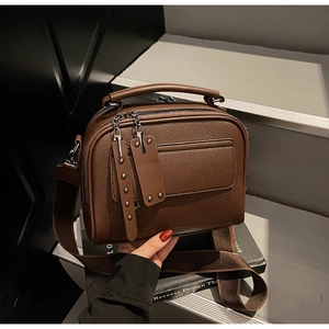 Detail view of dark brown pebbled leather crossbody bag with wide strap on grey steps