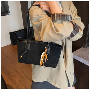 Detail of black quilted tote bag with wooden bead tassel charm on a beige trench coat