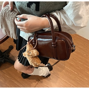 Close-up of a vintage brown leather bowling bag featuring a cute teddy bear plush charm
