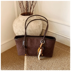 Detail of dark brown quilted tote bag with suede texture and wooden beaded tassel