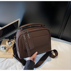 Detail view of dark brown pebbled leather bag with double zippers and metal rivet hardware