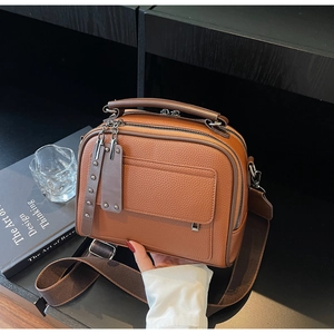 Close-up of brown litchi pattern leather bag with wide strap and metallic zippers
