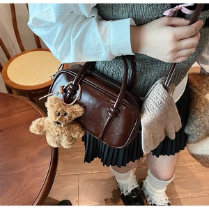 Close-up of a vintage dark brown patent leather handbag with a cute plush bear charm