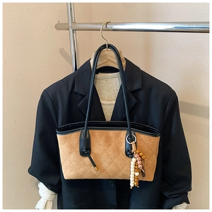 Detail of a brown quilted suede tote bag with black leather handles and beaded charm decor