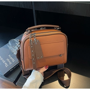 Close-up of brown litchi grain leather bag featuring double zippers and wide fabric strap