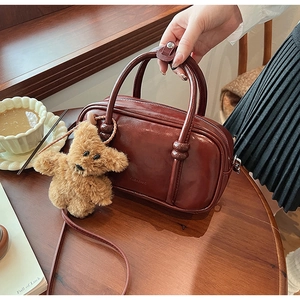 Retro burgundy bowling bag with polished finish and brown teddy bear charm on wood table