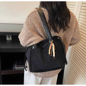 Detail of black suede drawstring bucket bag with colorful wooden bead charm and strap