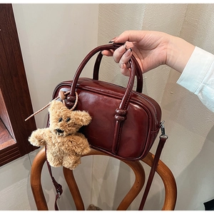 Detail of burgundy bowling bag with glossy finish and brown teddy bear charm accessory