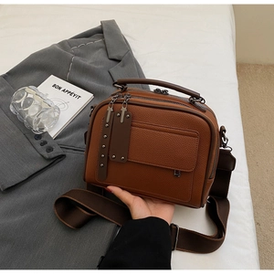 Detailed view of brown lychee grain leather square bag with dual zippers and wide strap