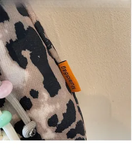 Close-up of leopard print crossbody bag with orange logo tag and decorative beads