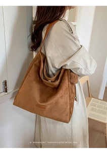 Close-up of minimalist brown suede tote bag with plush ball charm and logo detail