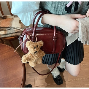 Detail of burgundy patent leather Boston bag with a cute brown teddy bear charm attached