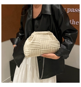 Detail of off-white woven texture and silver chain strap on shell-shaped clutch bag