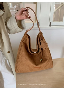 Detail of a large brown suede tote bag with a plush bear charm and beaded drawstring cord
