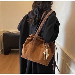 Detail view of brown faux suede tote bag with drawstring closure and beaded charm