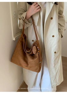 Brown suede tote bag with decorative tassel and pom-pom detail on model's shoulder