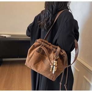Detail of brown faux suede bucket bag with wooden bead charm on a model in a modern interior