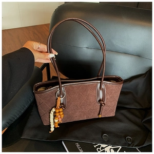 Detail of dark brown quilted tote bag with suede texture and wooden bead tassel charm