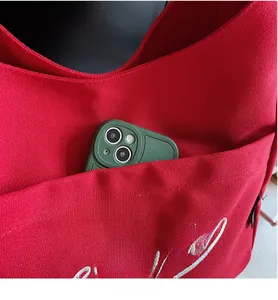 Detail of red canvas tote bag with white embroidery and external pocket holding a phone