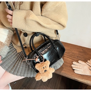 Glossy black patent leather mini bowling bag with a cute plush bear charm on a wooden bench