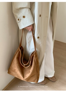 Detail of a large brown suede tote bag styled with a minimalist beige trench coat
