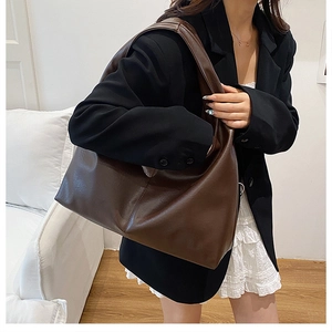 Side view of large brown faux leather tote bag worn as a shoulder bag on a model
