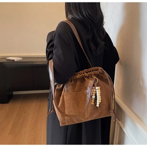 Close-up of brown suede drawstring bucket bag with leather strap and beaded tassel detail