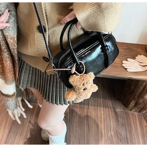 Detail of a black glossy mini bowling bag featuring a cute plush bear charm on handles